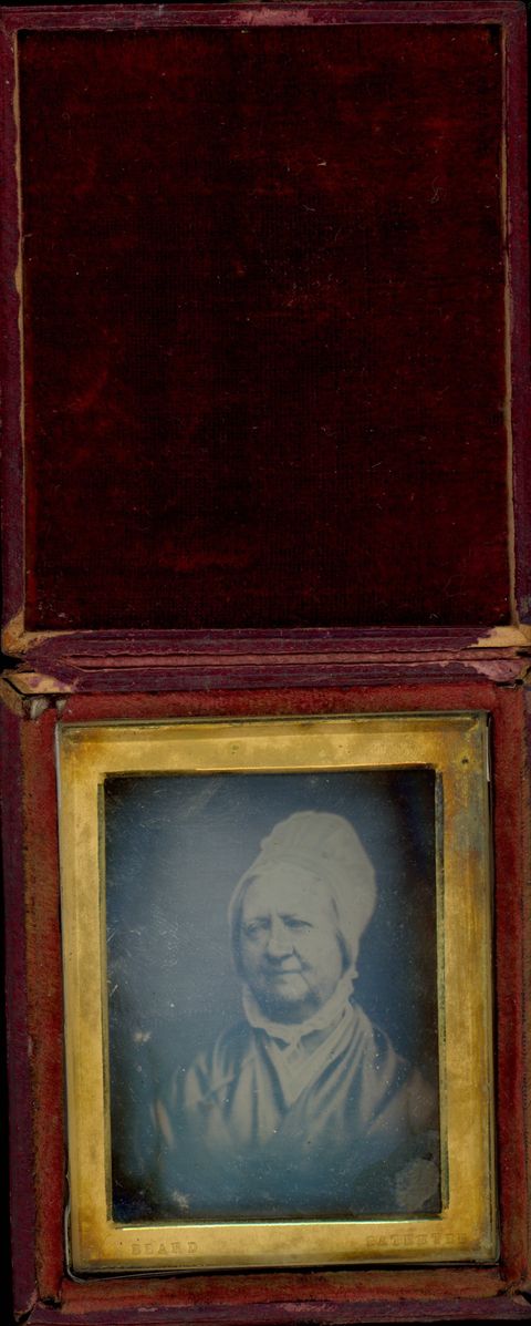 Daguerreotype in an open case. A pale-skinned woman with rounded cheeks and sagging jowls looks off to our left in a rectangular gold mat set in a red case. The words “Beard” and “Patentee” are stamped into the bottom corners of the gold mat.